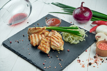 Appetizing chicken kebab with spices and onions on a black slate tray on a white background. Shahlik. Close up portion of grilled meat