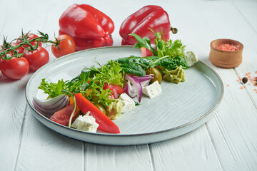 Light, diet salad with red onion, lettuce, spinach, tomatoes, bell pepper and feta cheese in a beautiful plate on a white wooden background