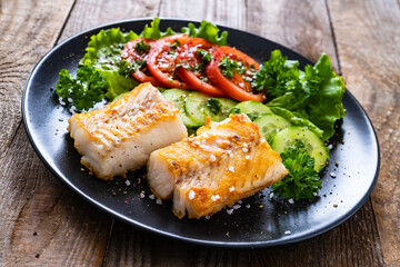 Fish dish - fried cod fillet with vegetables on wooden table
