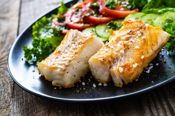 Fish dish - fried cod fillet with vegetables on wooden table
