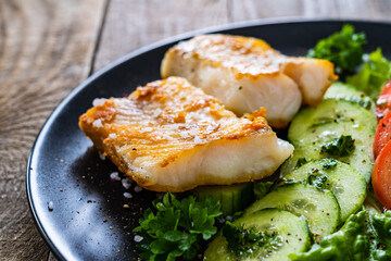 Fish dish - fried cod fillet with vegetables on wooden table
