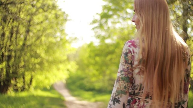 Video clip, blur effect and light fler, a young blonde woman with long hair in a long dress walks in a blossoming apple orchard on a sunny day in spring.