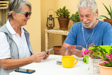 Two retired people playing cards outdoor on the terrace. Cell phone and tablet on the table. Happy retirement concept