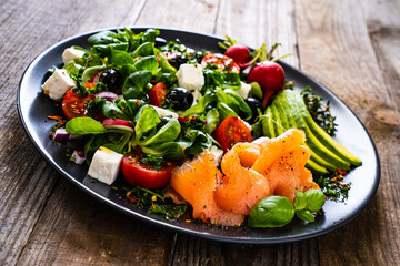 Breakfast - smoked salmon, feta cheese, avocado and vegetable salad on wooden table
