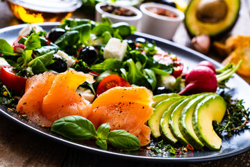 Breakfast - smoked salmon, feta cheese, avocado and vegetable salad on wooden table
