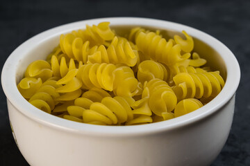 Italian Fusilli or Rotini helix shaped Macaroni Pasta in white bowl with dark background.