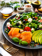 Breakfast - smoked salmon, feta cheese, avocado and vegetable salad on wooden table
