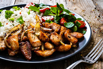 Chicken meat with rice and vegetables on wooden table

