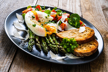 Boiled egg with bread, asparagus, parmesan and vegetable salad on wooden table