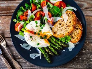 Boiled egg with bread, asparagus, parmesan and vegetable salad on wooden table