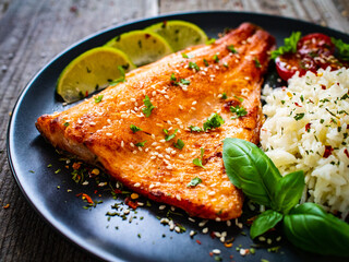 Fried salmon steak with rice and vegetables on wooden table
