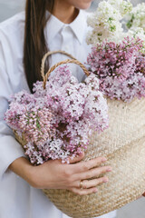The girl holds in her hands a wicker basket with flowers. Basket with lilacs. Girl and flowers. Walk with a basket of lilacs in the hands. Floristics