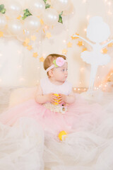 Cute little girl in a pink princess dress with a flower on her hair plays with wooden ballerinas among the golden stars on the background of a large white wooden moon and balloons. Children's decor. 
