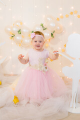 Cute little girl in a pink princess dress with a flower on her hair plays with wooden ballerinas among the golden stars on the background of a large white wooden moon and balloons. Children's decor. 
