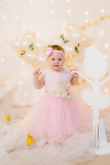 Fototapeta premium Cute little girl in a pink princess dress with a flower on her hair plays with wooden ballerinas among the golden stars on the background of a large white wooden moon and balloons. Children's decor. 