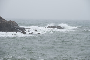 High tides crashing waves on the Maine coast on a rainy and foggy day