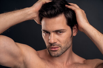 Handsome young bearded man isolated. Portrait of shirtless muscular man is standing on grey background and holding his hair.