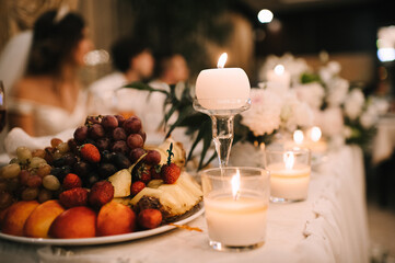 Fototapeta na wymiar Fruits on a plates, Grapes, pineapple, strawberries, peach, plum. Reception, catering. The table is covered with a white tablecloth. Candles are burning