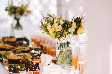 Bouquet of white, yellow, green flowers in a glass vase. Reception, catering. The table is covered with a white tablecloth.