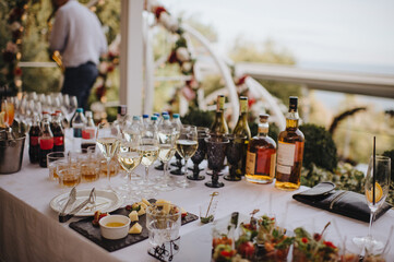 Glasses and bottles with white wine, whiskey. Plate with assorted cheese. Reception, catering. The table is covered with a white tablecloth.