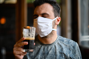 Young man trying to drink a beer wearing a mask, funny coronavirus concept