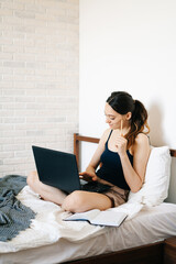 A young woman, using a laptop, communicates over the Internet with a client in her bed, while the virus is quarantined.Cozy office workplace,Remote work, e-learning concept.freelancer