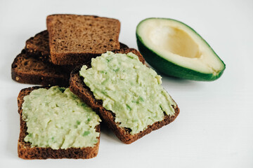 Slices of brown bread with avocado on a white wooden table. Copy, empty space for text