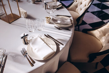 Table setting for a wedding party. a round table with a white tablecloth, glasses, white plates in the rays of the setting sun.