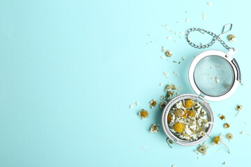 Dry chamomile flowers in infuser on light blue background, flat lay. Space for text