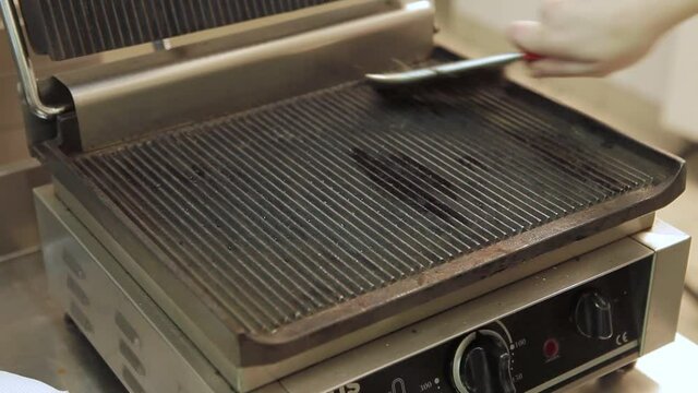 Dirty electric grill. Male hand wiping with cloth grill. Cleaning electric grill dirty plate with rag, detail on man hand. Fry on electric roaster rosemary black pepper salt.