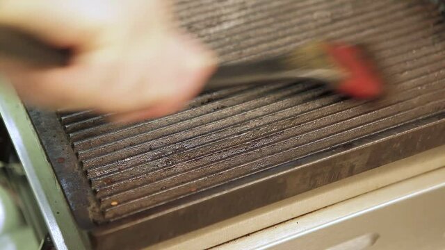 Dirty electric grill. Male hand wiping with cloth grill. Cleaning electric grill dirty plate with rag, detail on man hand. Fry on electric roaster rosemary black pepper salt. Closeup shot
