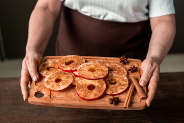 Hands of mature female holding chopping board with pile of fresh apple slices