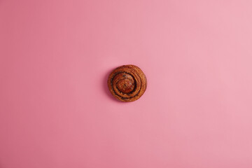 Homemade delicious appetizing cinnamon bun with caramelized sugar and jam filling isolated on pink background. Ready to eat sweet tasty swirl roll. Bakery, nutrition, unhealthy food concept.