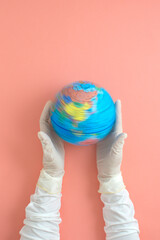 Women hands wearing surgical glove holding on spinning planet earth on pink background