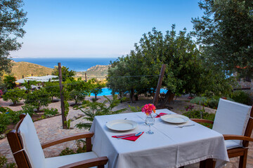 close up dinner table on the outside with a sea view, red flower and plates on table