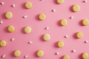 Sweet round yellow macaroons with white marshmallow on pink studio background. Colorful pattern french cakes. Cookies dessert containing much calories and sugar. Temptation, sweet tooth concept