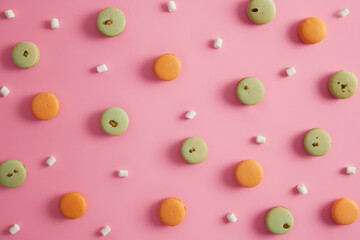 Photo of sweet delicacy green and orange macaroons with pistachio. Delicious marshmallow on pink background around yummy french cookies. Colorful tasty dessert for sweet tooth. Unhealthy eating