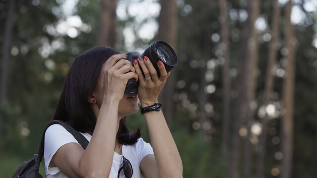 Traveler photographing scenic view in forest. One caucasian woman shooting close up look. Girl take photo video on dslr mirrorless camera. Professional photographer travel with backpack. Outdoor.
