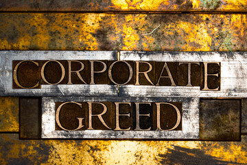 Photo of real authentic typeset letters forming Corporate Greed text on vintage textured silver grunge copper and gold background