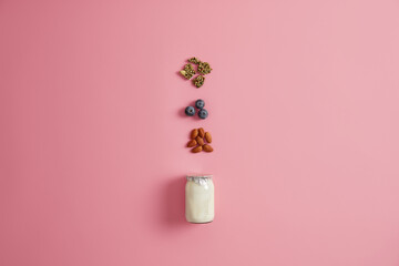 Yoghurt, pumpkin seeds, blueberry and almond nut on pink studio background. Ingredients for healthy nourishing breakfast. Preparing delicious snack. Balanced dieting and proper nutrition concept