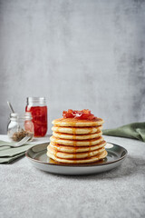 American-style pancakes with apple jam in muted green plate on grey background. A jar of jam, tea, green napkin on the background. Fork on another napkin near the plate