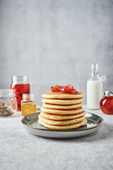 American-style pancakes with apple jam in muted green plate on grey background. Jars with jam, honey and tea leaves, bottle of milk on the background
