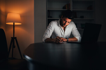 Young man working on computer at night in dark office. Business man working late at night from home / office