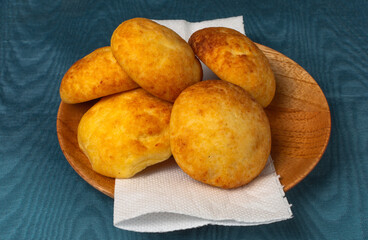 Typical colombian almojabanas, traditional colombian cheese bread over a wood plate with napkin on blue background. Traditional bakery