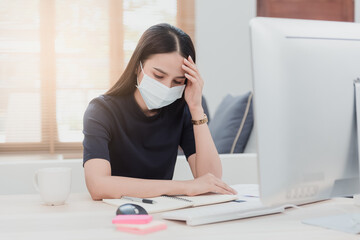 Asian women are working from home. With illness, respiratory illness, wearing a medical mask, her hands touched on his forehead. Have a headache In front of the computer