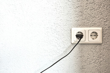 Double electrical power European socket with black cable and plug on white wall space for text