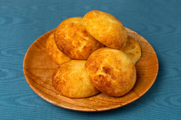 Typical colombian almojabanas, traditional colombian cheese bread over a wood plate on blue background. Traditional bakery