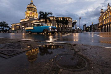 Old car on streets of Havana with Capitolio building in background with reflection on rain time. Cuba