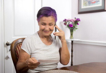 Joyful senior woman talking on cell phone reading a memory card - 353906841