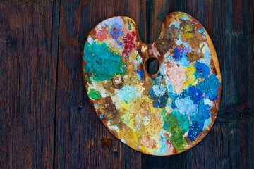 A colourful palette with dry tempera colours on it, hung on a wood wall.